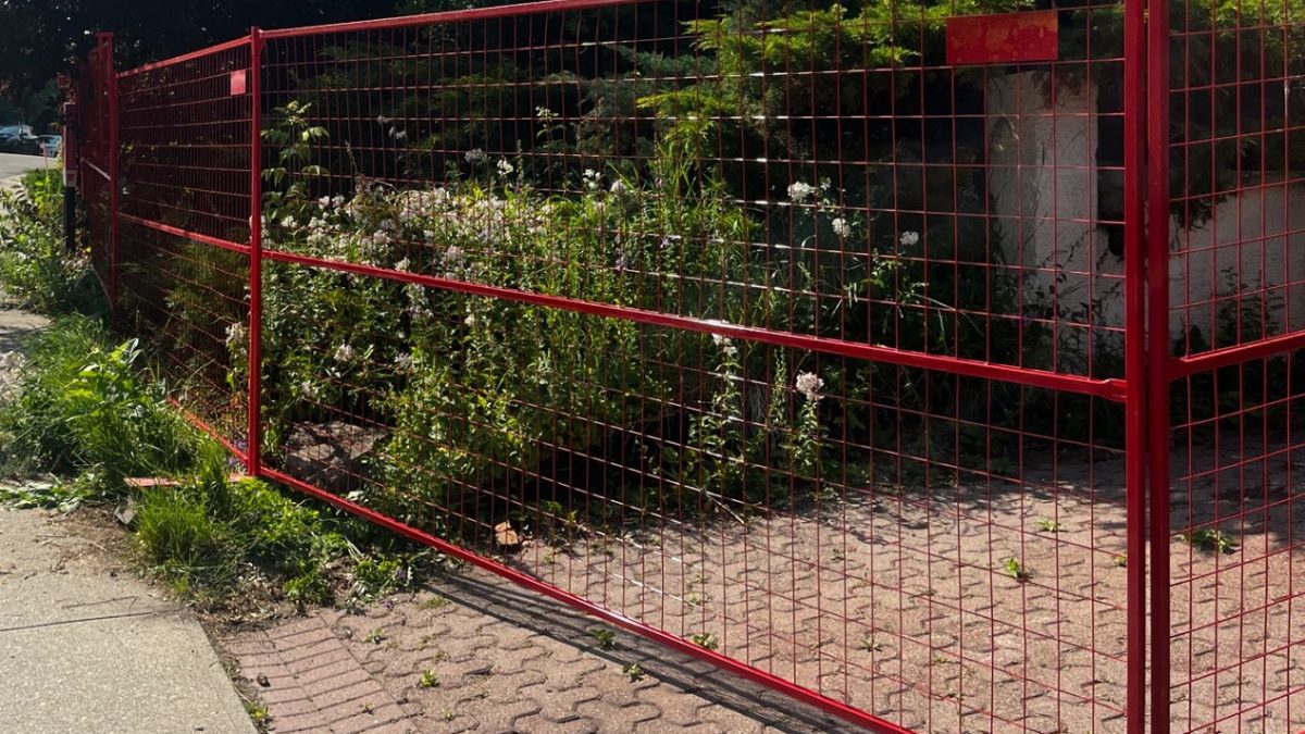Red temporary fence panels along a sidewalk at an infill construction site