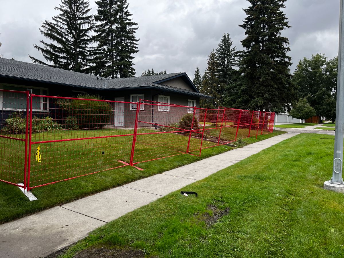 Red temporary fence panels along a sidewalk in front of a house