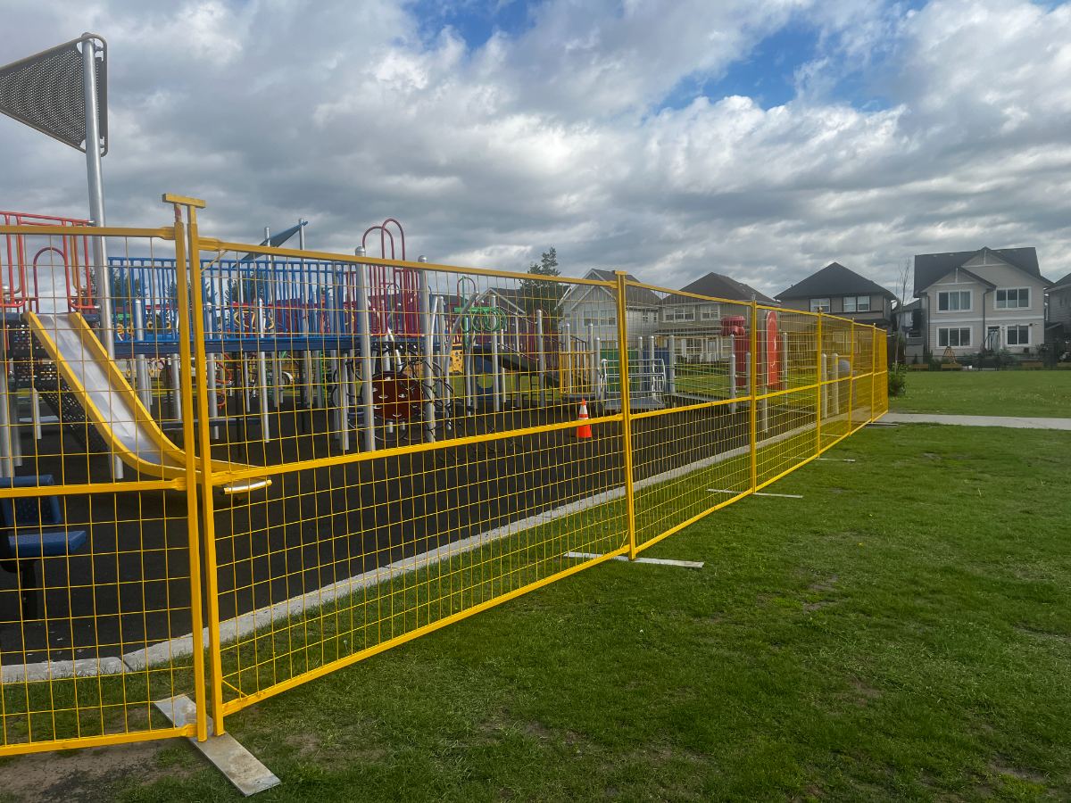 Red temporary fence panels around a school field near a playground climber