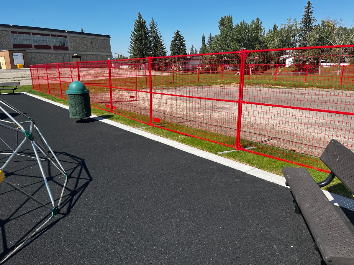 Yellow temporary fence panels enclosing a playground slide and climbing structure