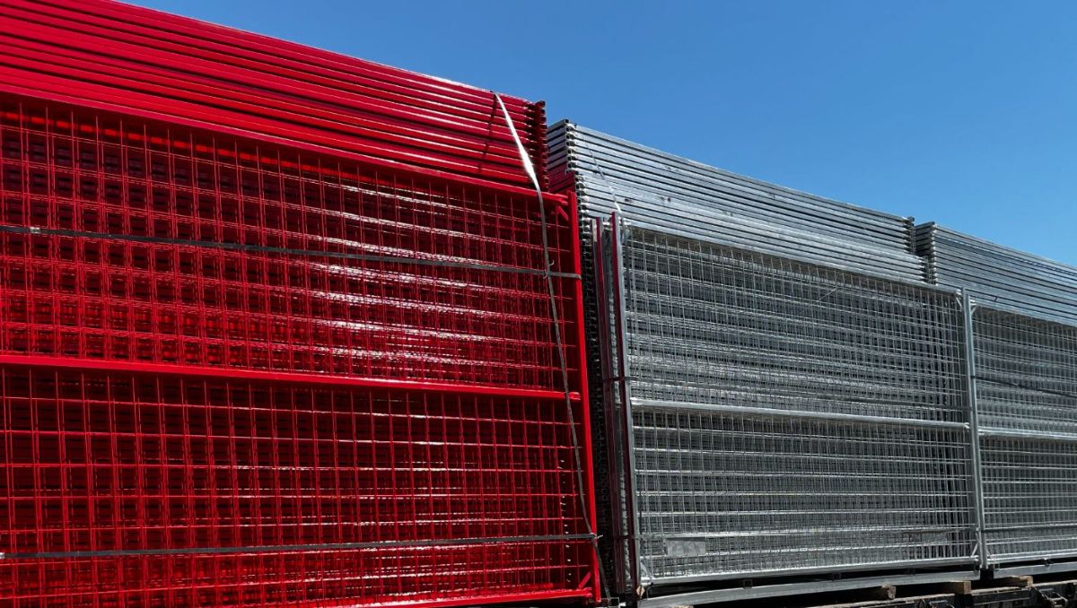 Stacks of red and galvanized temporary fence panels against a clear sky