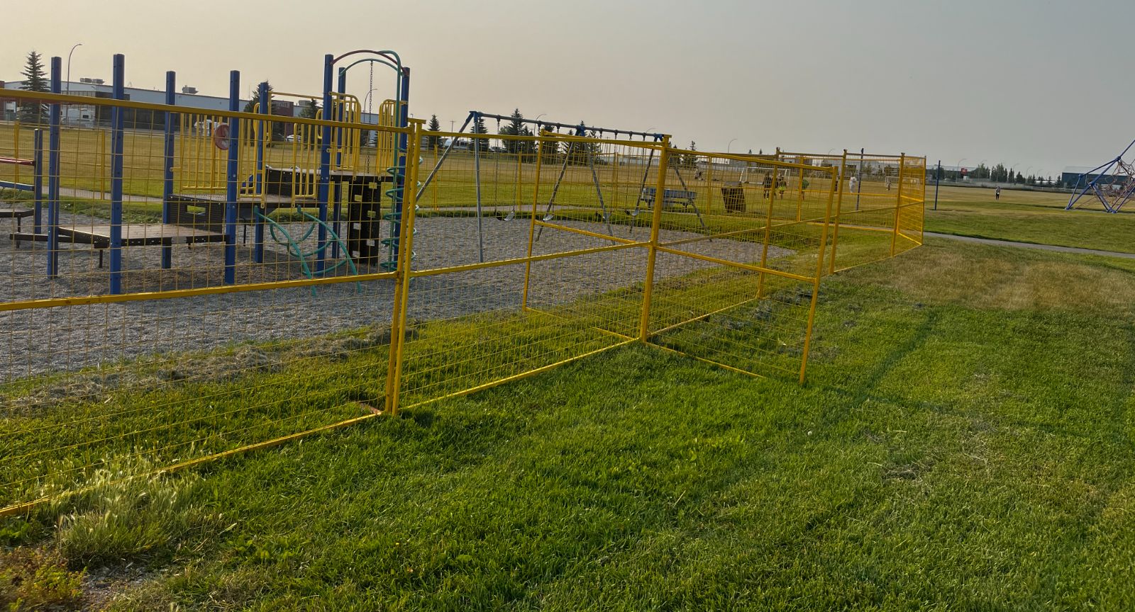 Yellow temporary fence panels enclosing a playground and swing set