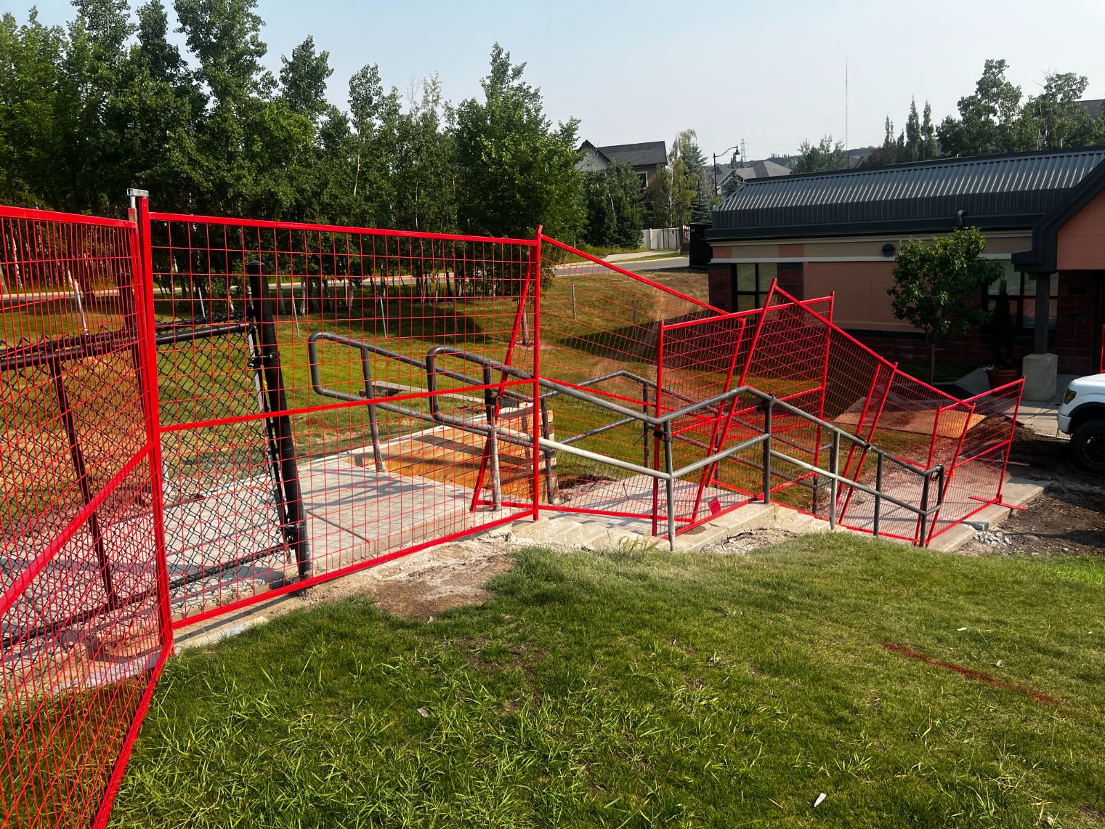 Red temporary fence panels secured around outdoor stairs and a railing