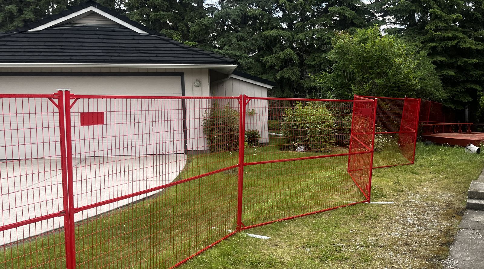 Red temporary fence panels enclosing a residential driveway and garage